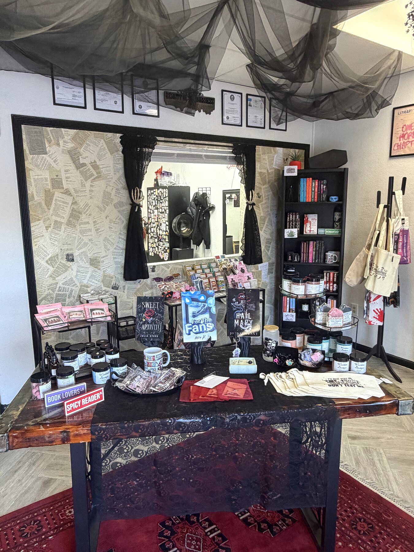 Display table with indie romance books, Til Death candles and tote bags under draped tulle